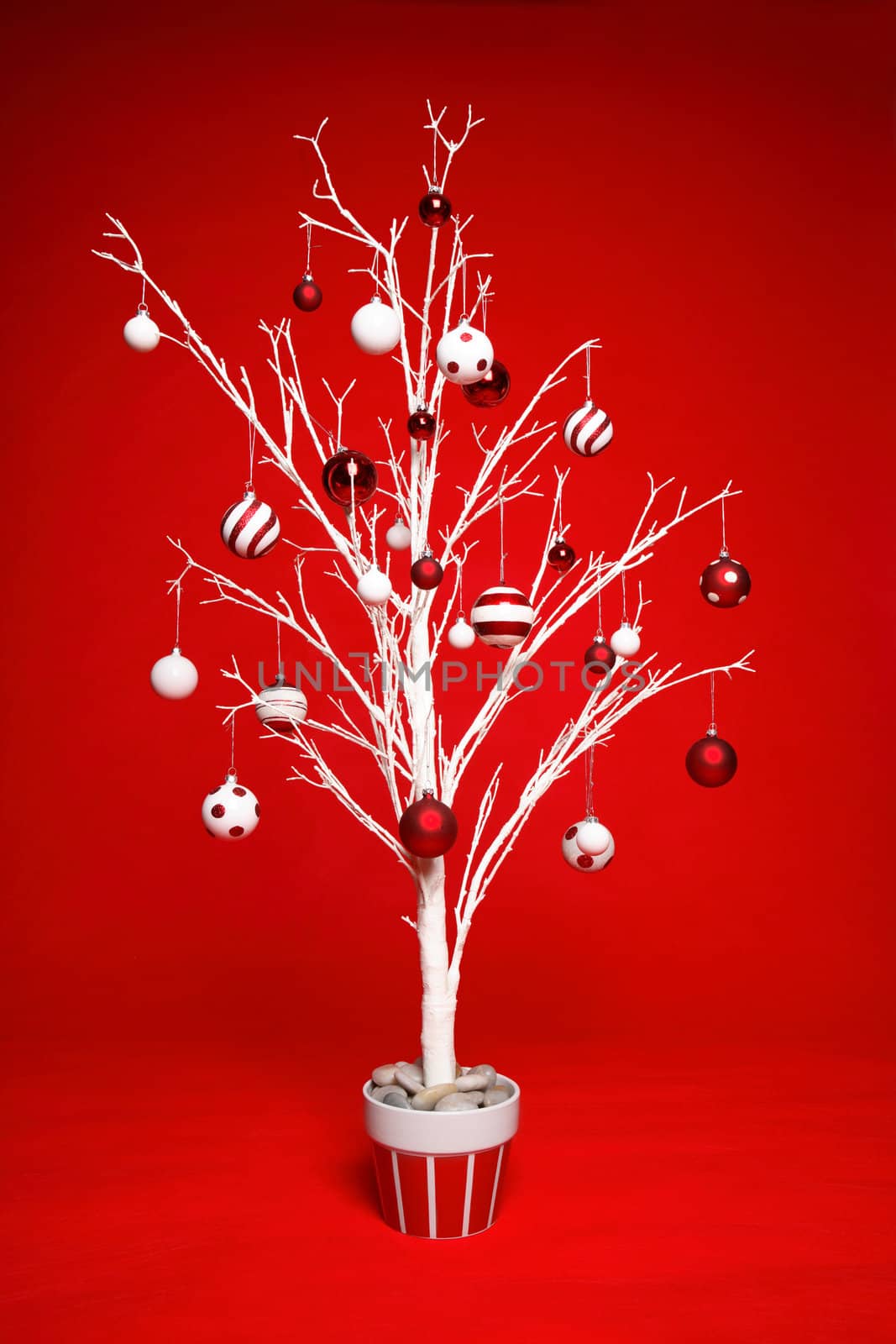 White modern Christmas tree decorated with various red and white themed christmas baubles (balls) on a red background.