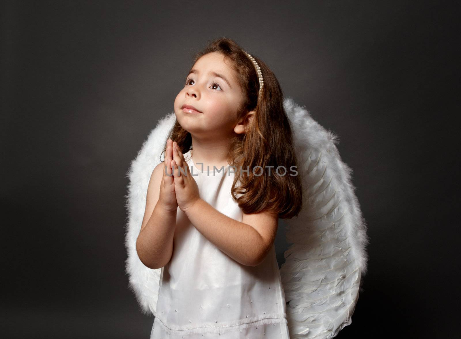 Little white angel child with hands together in devotional prayer and looking heavenward with hope and faith.