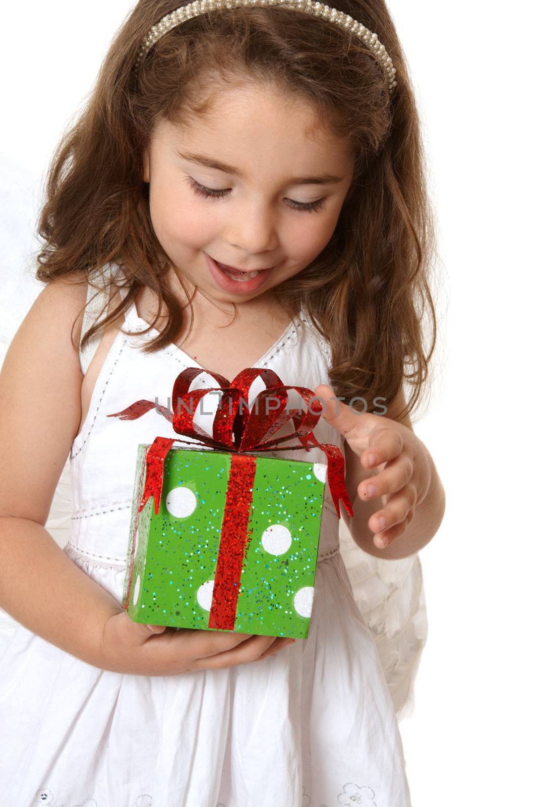 A little girl with browin hair looks down in delight at a Christmas present