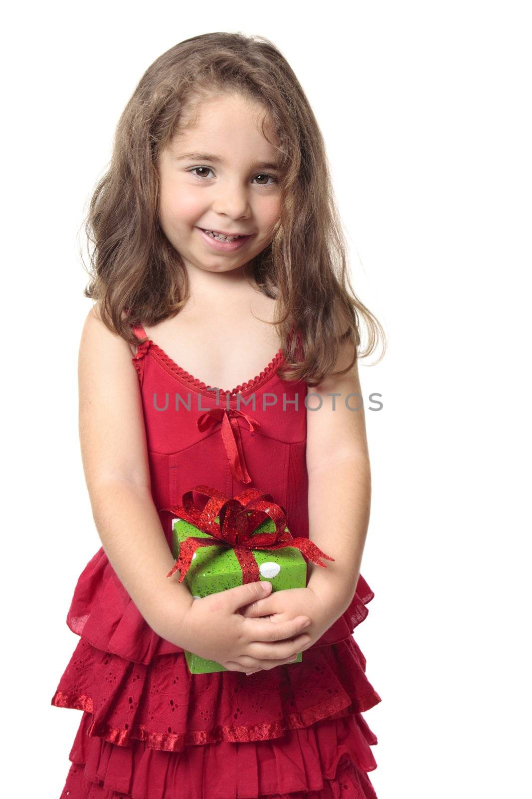 Little girl in a red dress holds a green and red present and smiles sweetly.