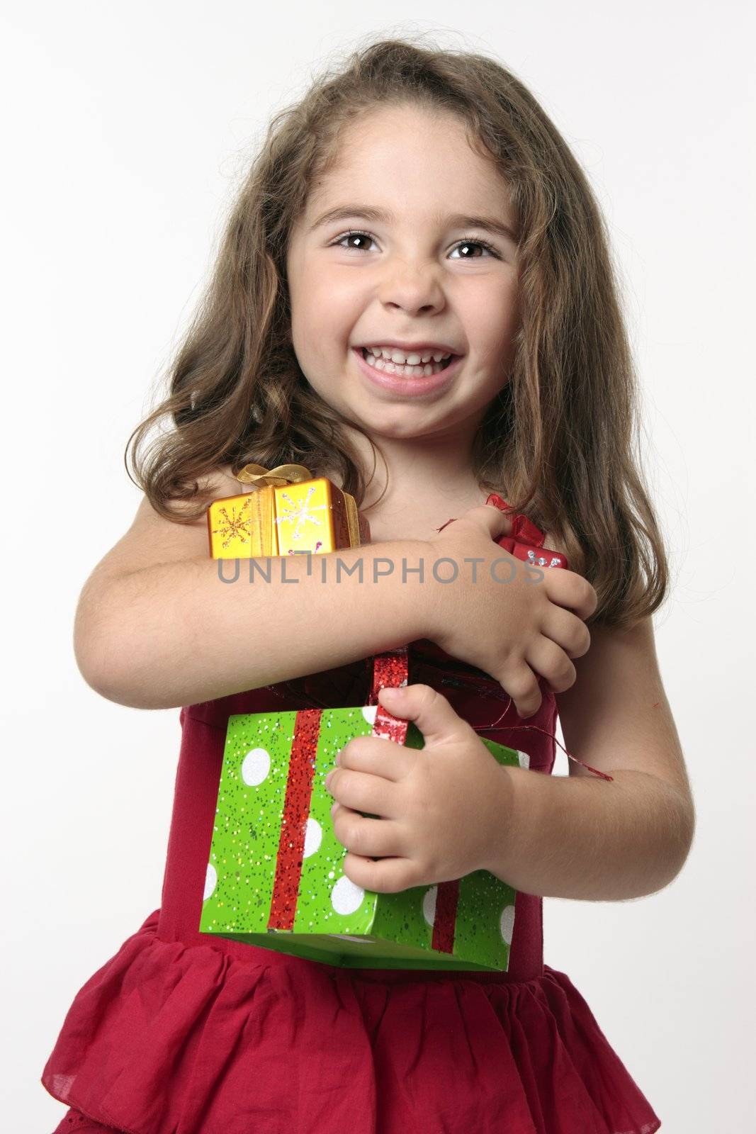 Pretty young girl in a red dress, is holding presents and giggling with excitement and  happiness.