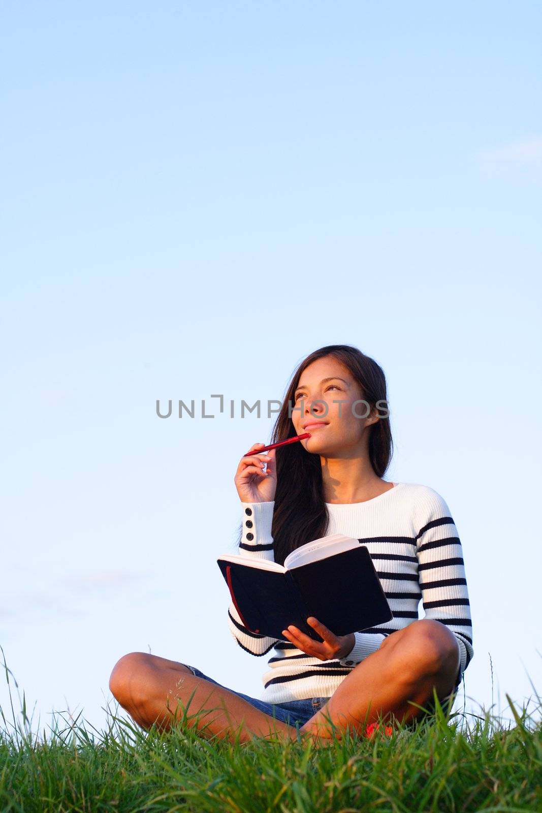 Woman thinking hard studying outside in evening light with a lot of copy space. Beautiful mixed asian / caucasian woman.