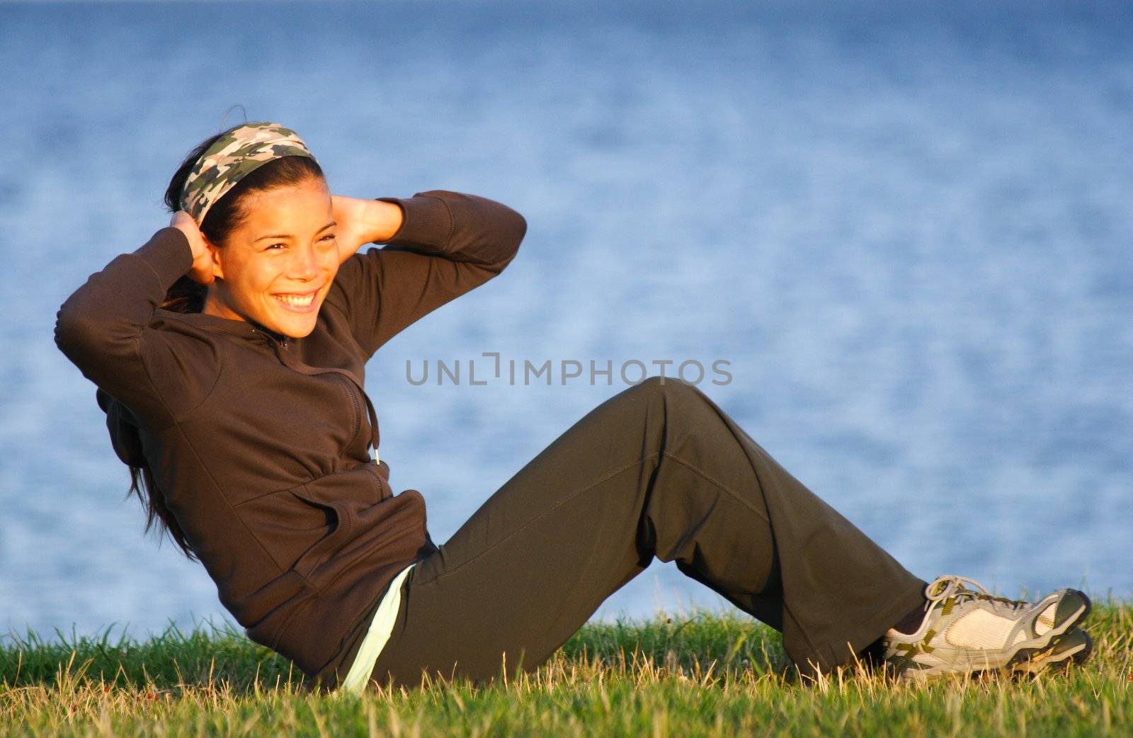Woman doing situps / exercise outdoors on grass with the ocean in the background