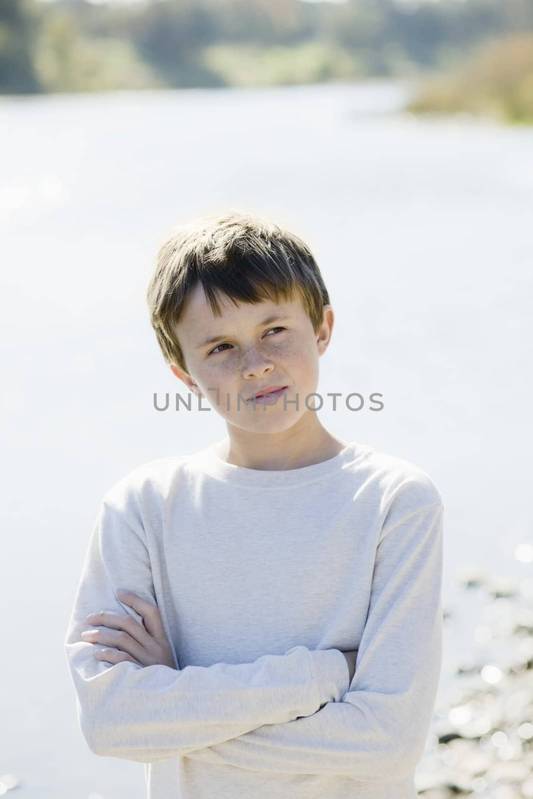 Cute Young Boy Standing By a River With Arms Crossed Looking Away From Camera