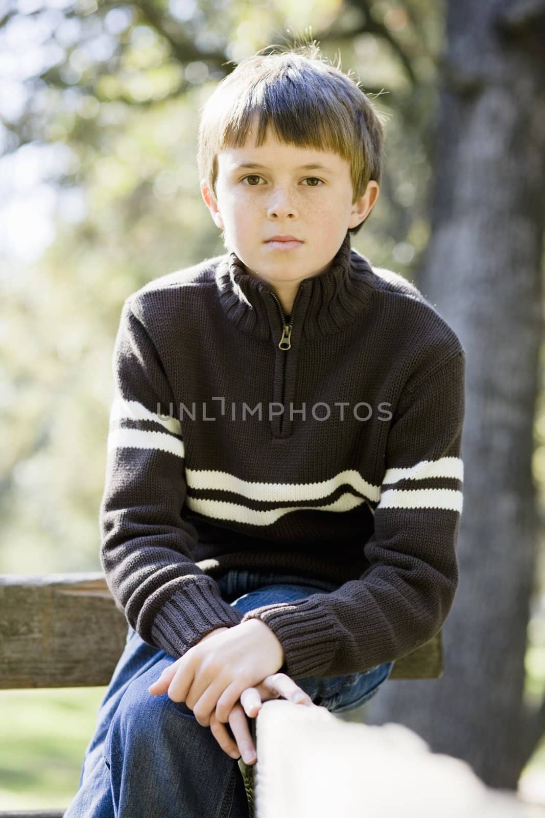 Portrait of a Cute Young Boy Sitting on a Wooden Railing Looking Directly To Camera