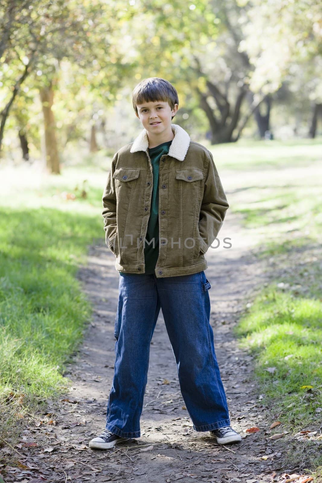Cute Young Boy Standing with Hands in Pockets on a Path in a Park