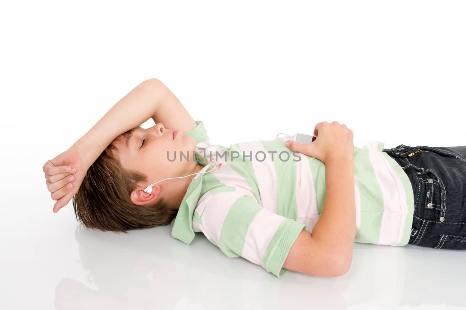 A young boy lying down listening to music on a digital portable mp3 player.