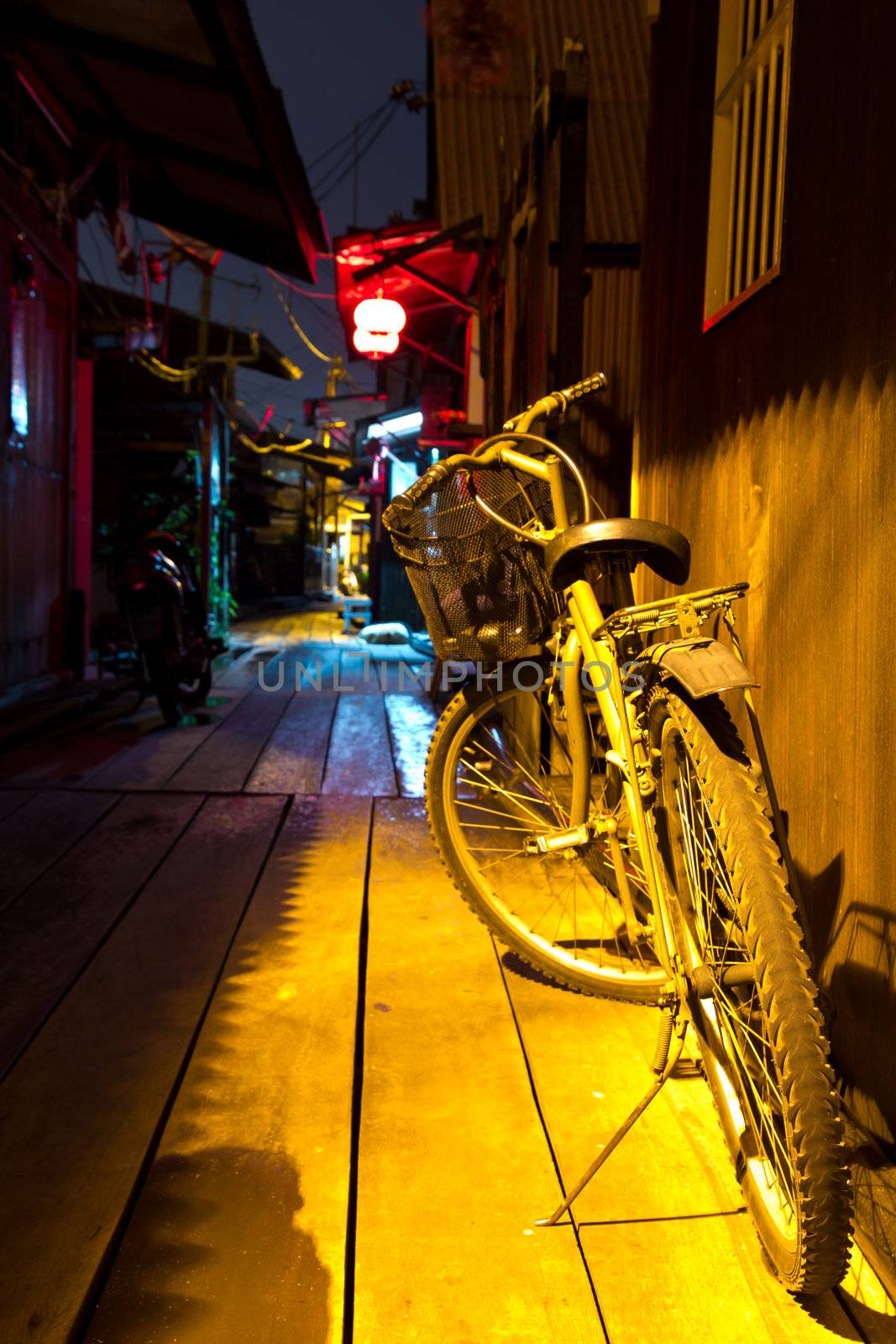 Old bicycle against wooden wall under amber light at night in a quiet street