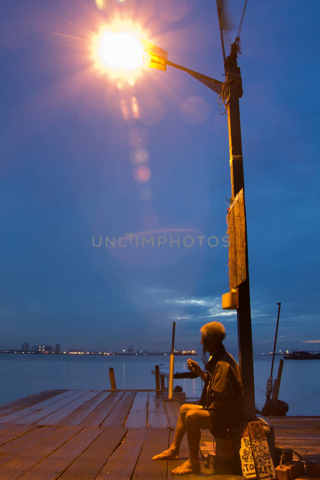 Lonely old man under a lamp pole smoking