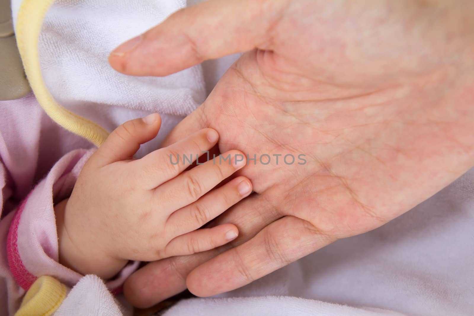 Baby hand in mother's palm against white blanket