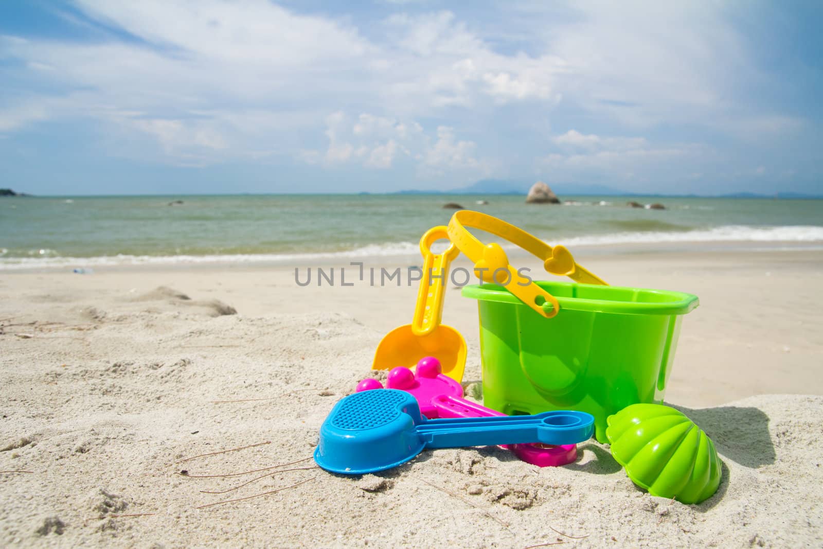 Child's bucket, spade and other toys on tropical beach against blue sky