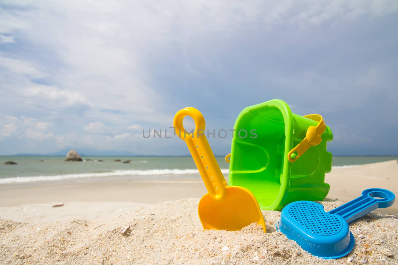 Child's bucket, spade and other toys on tropical beach against blue sky