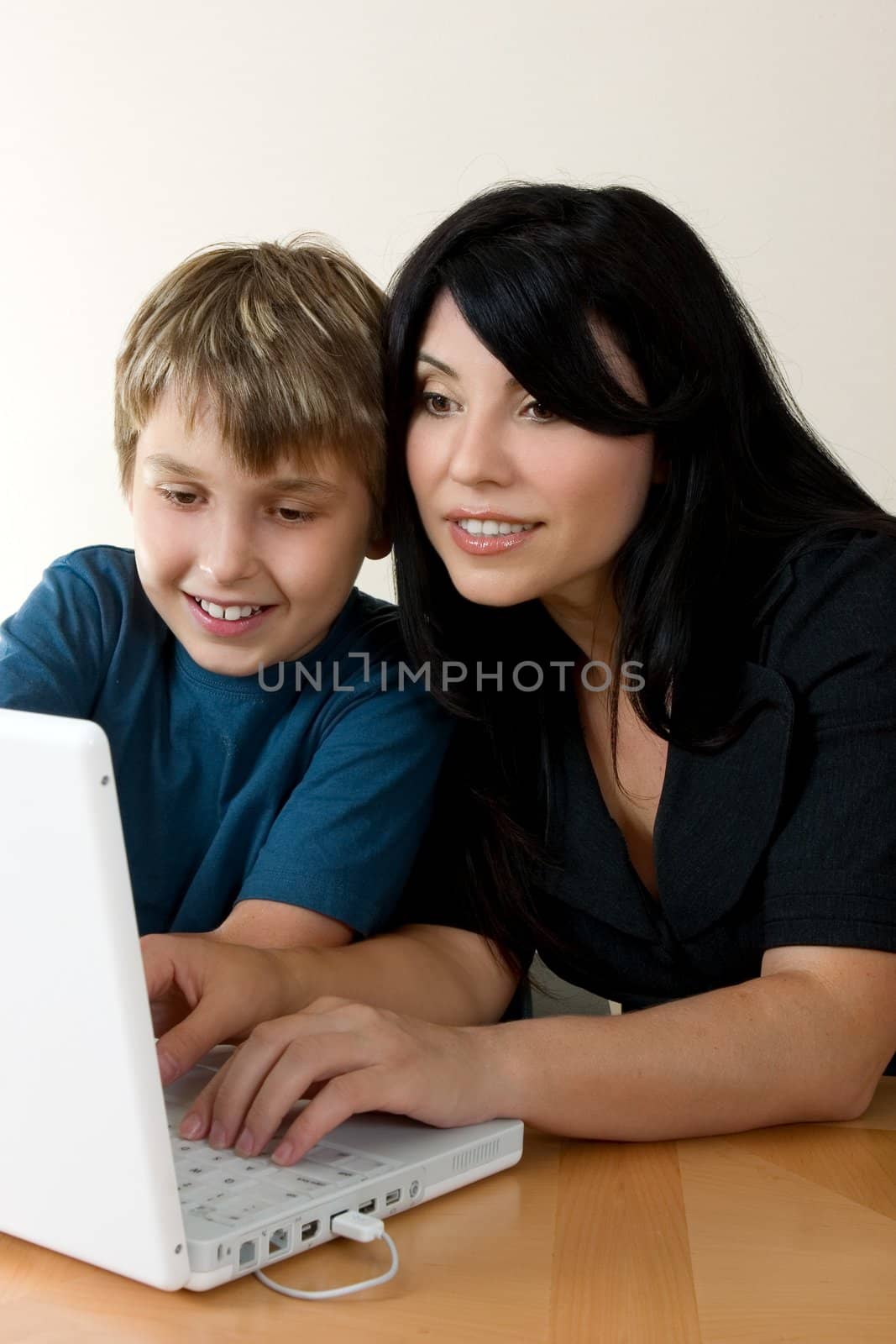 A woman using a computer while a child happily, ooks on.