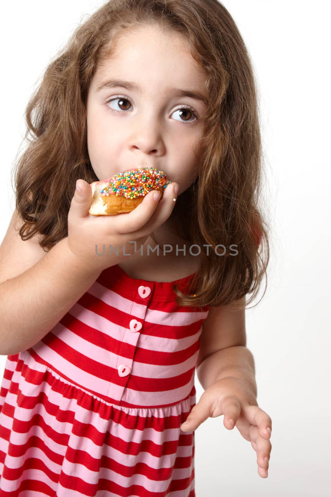 Little girl in a light pink and red striped dress eats a tasty pink iced decorated doughnut 