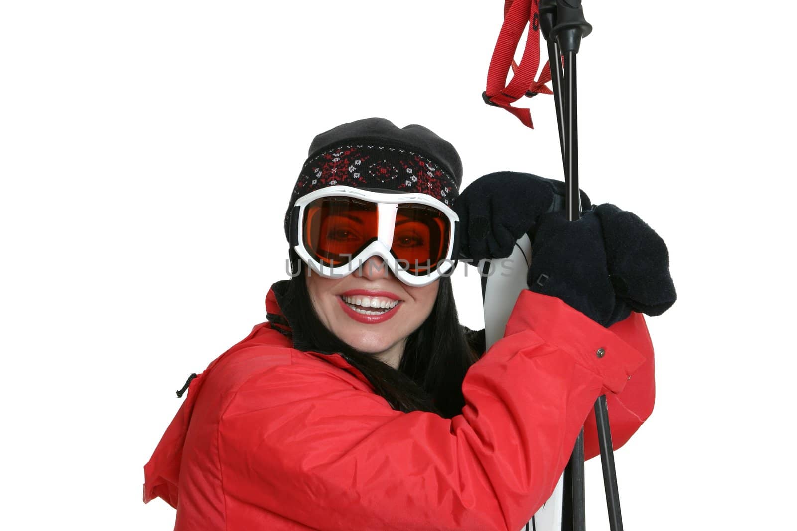 Female skier wearing warm red parka, beanie and goggles is leaning on skis and smiling.