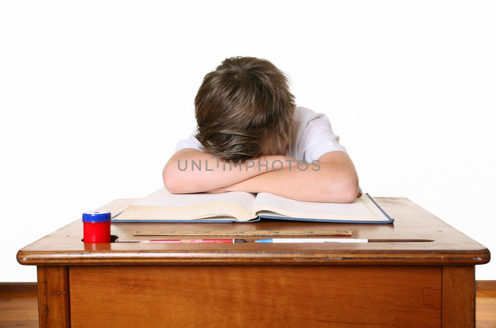 A unhappy or frustrated schoolboy sitting at desk and bent over with head in hands