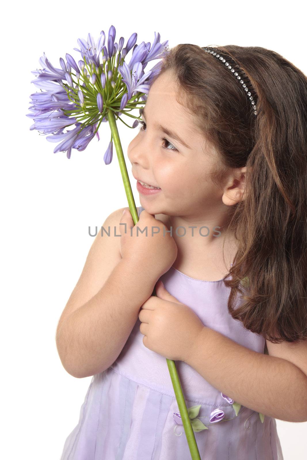 Pretty little  girl in purple mauve dress holding a beautiful agapanthus flower and smiling sweetly.