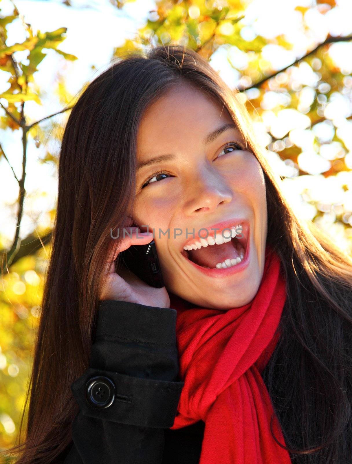 Woman on mobile phone closeup. Happy laughing young woman on cell phone outside in park. Beautiful mixed race caucasian / asian woman,