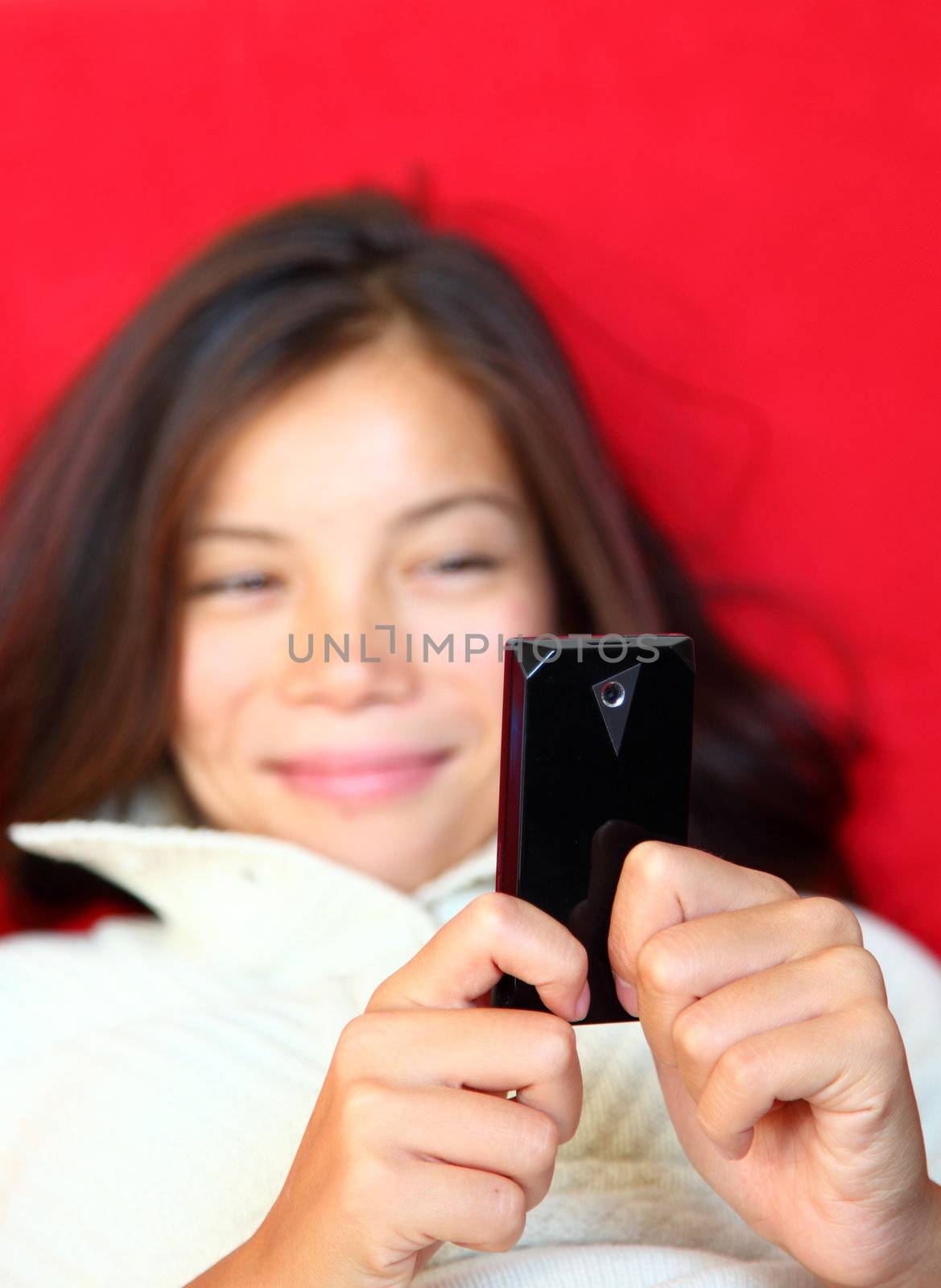 SMS on cellphone. Beautiful woman smiling being happy reading a sms on her mobile phone. Mixed race asian / caucasian model. Shallow depth of field, focus on phone.