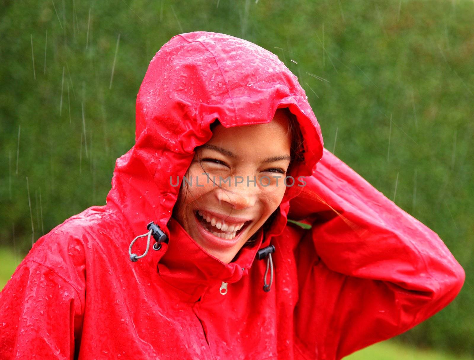 Rain woman. Beautiful young woman in red rain coat laughing having fun outside while it is raining heavily.