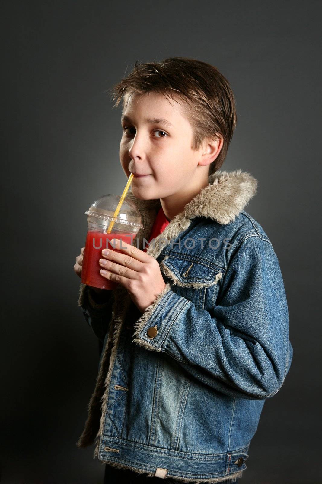 A young boy against a dark background, sips a tasty berry juice.