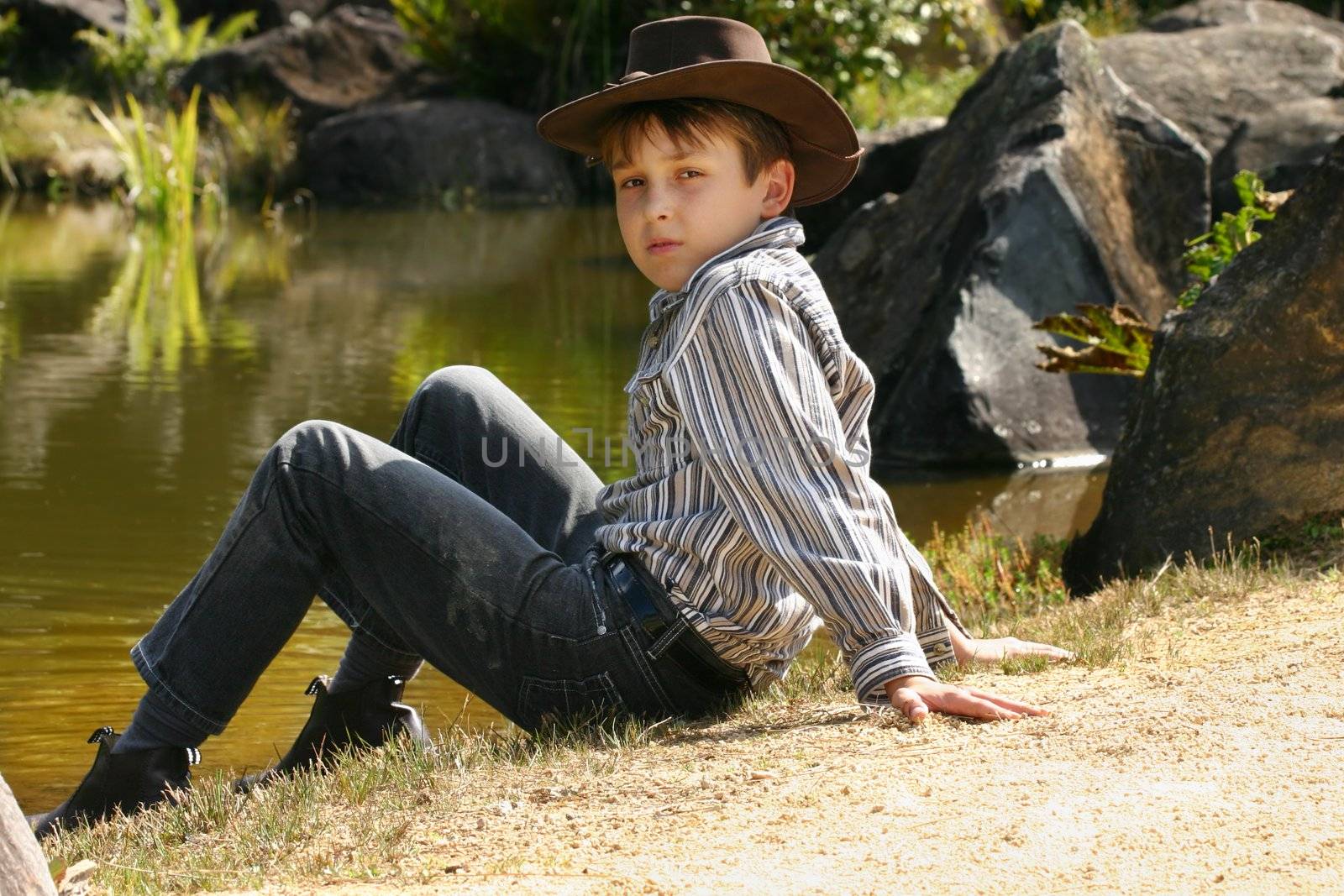 Rural boy sitting by banks of a river by lovleah