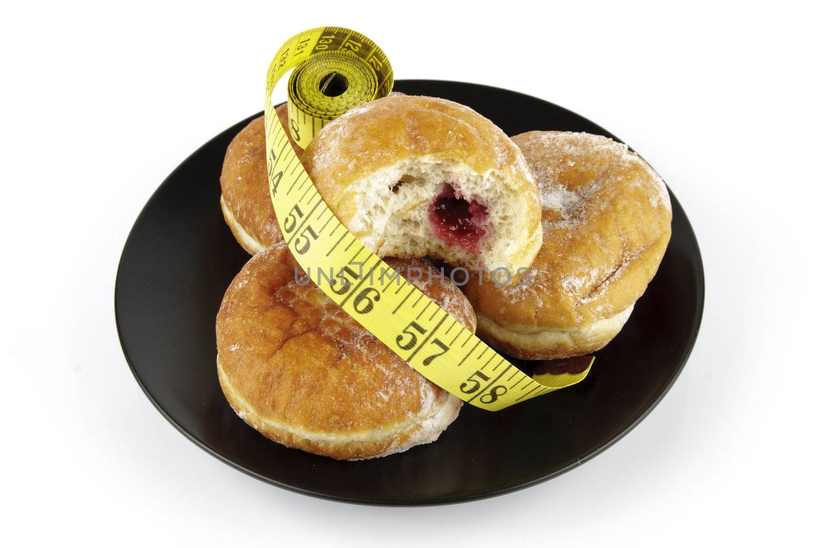 Black round plate of jam doughnuts with a yellow tape measure on a reflective white background