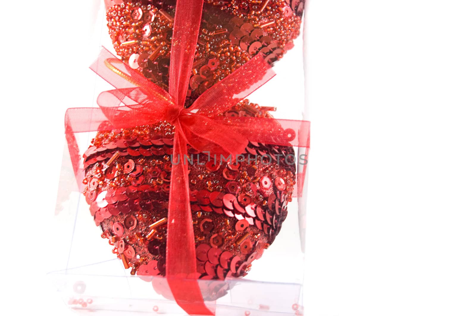 Two red hearts in transparent packing and beads over white