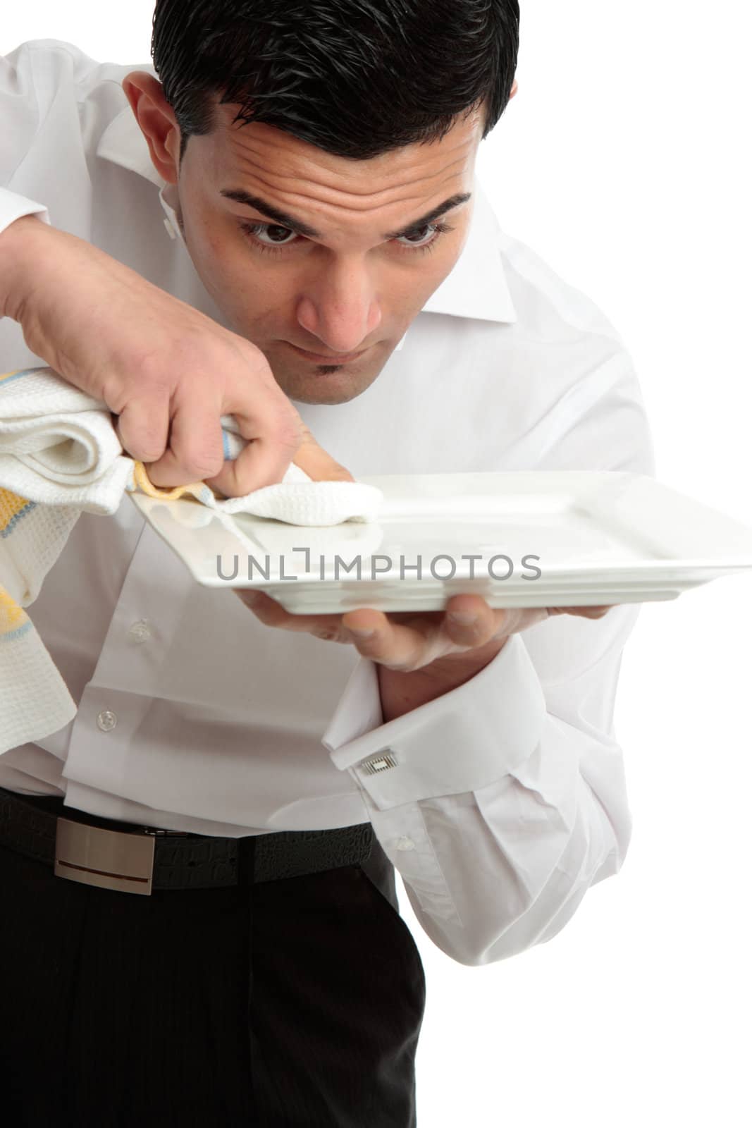 A male waiter servant or other hospitality staff worker is cleaning and polishing a white plate ready for service.