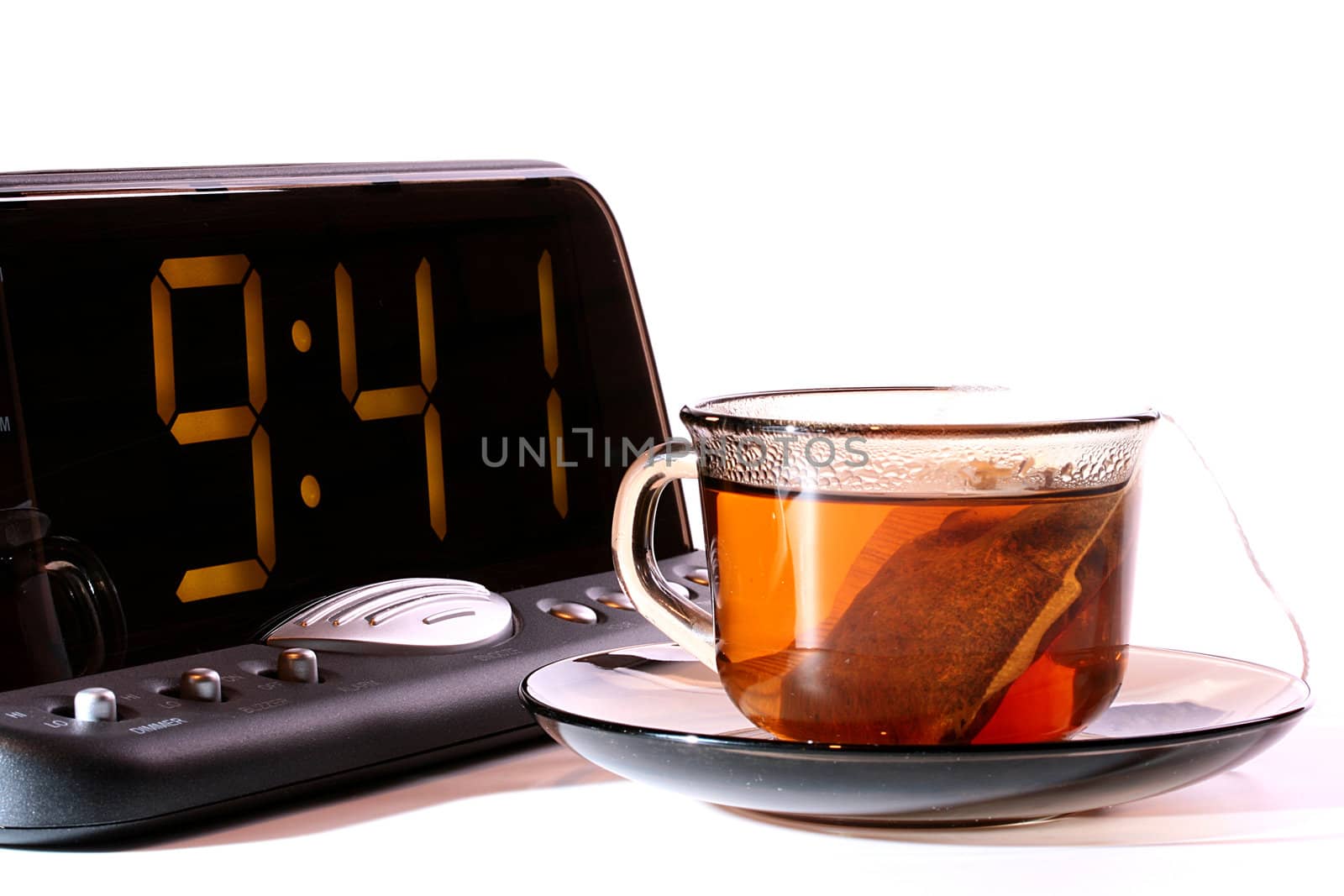 Electronic clock with a cup with tea in the foreground at office.