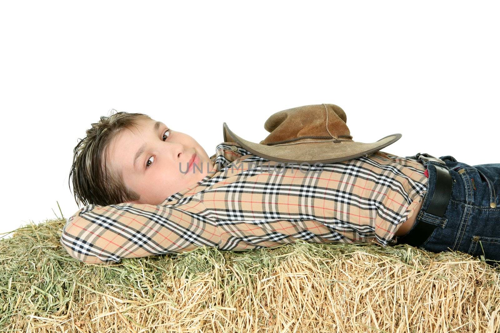 Country boy in checked shirt and jeans rests on a bale of lucern hay.