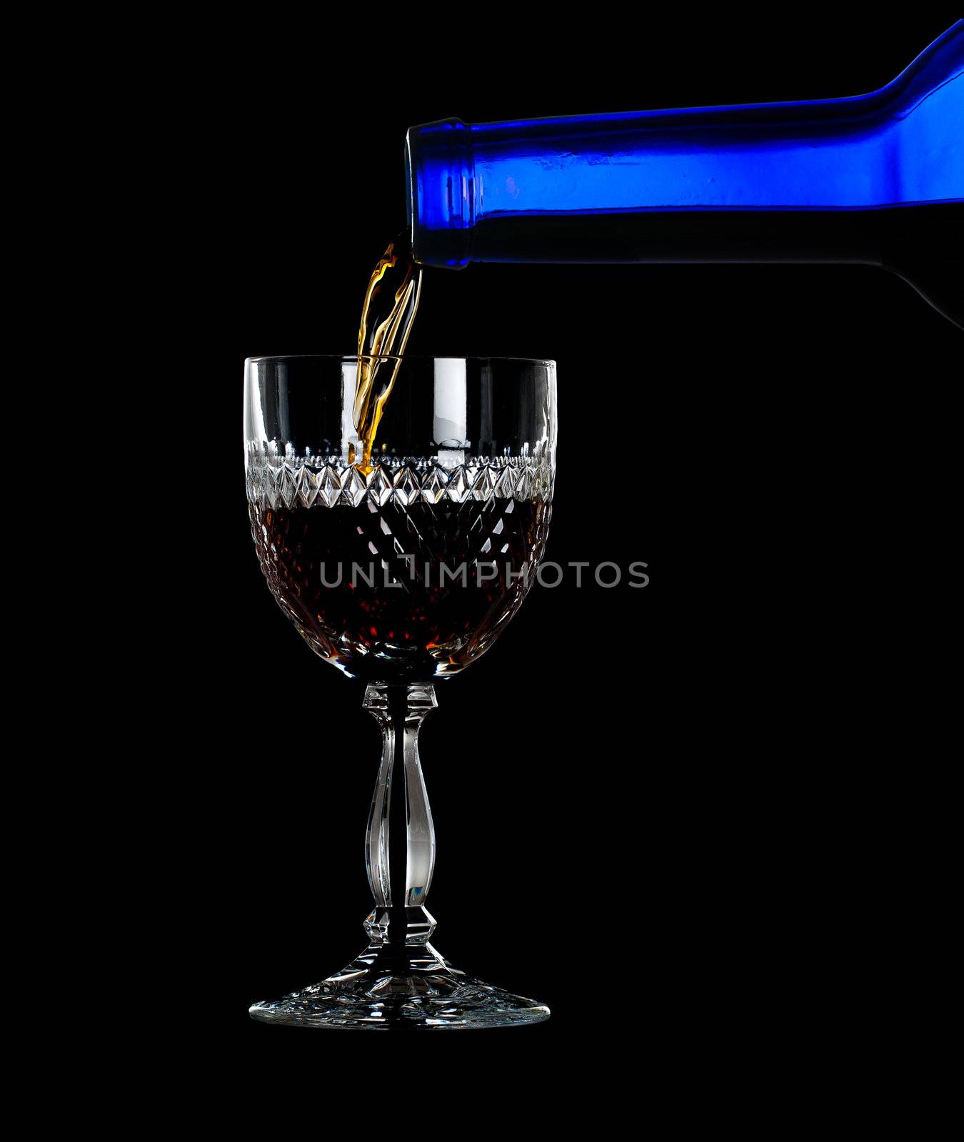 Sherry, port or whisky being poured from blue wine bottle into an elegant cut glass and isolated against black