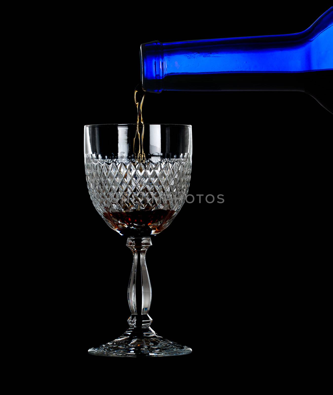 Sherry, port or whisky being poured from blue wine bottle into an elegant cut glass and isolated against black