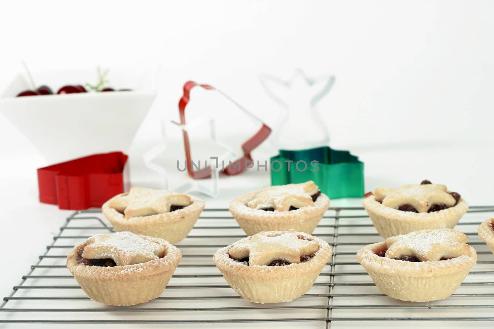 Small fruit tarts with festive star tops dusted with icing sugar sitting on a wire cooler.  
Focus on foreground.