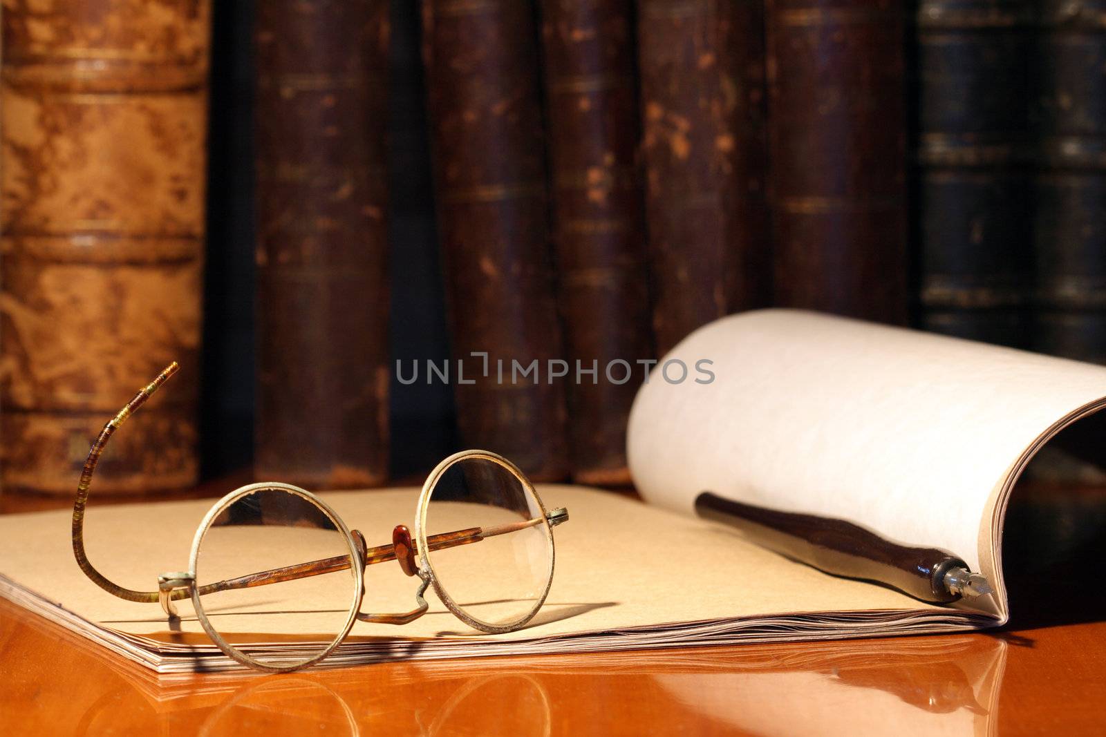 Vintage still life with old spectacles, paper notebook and pen on background with books