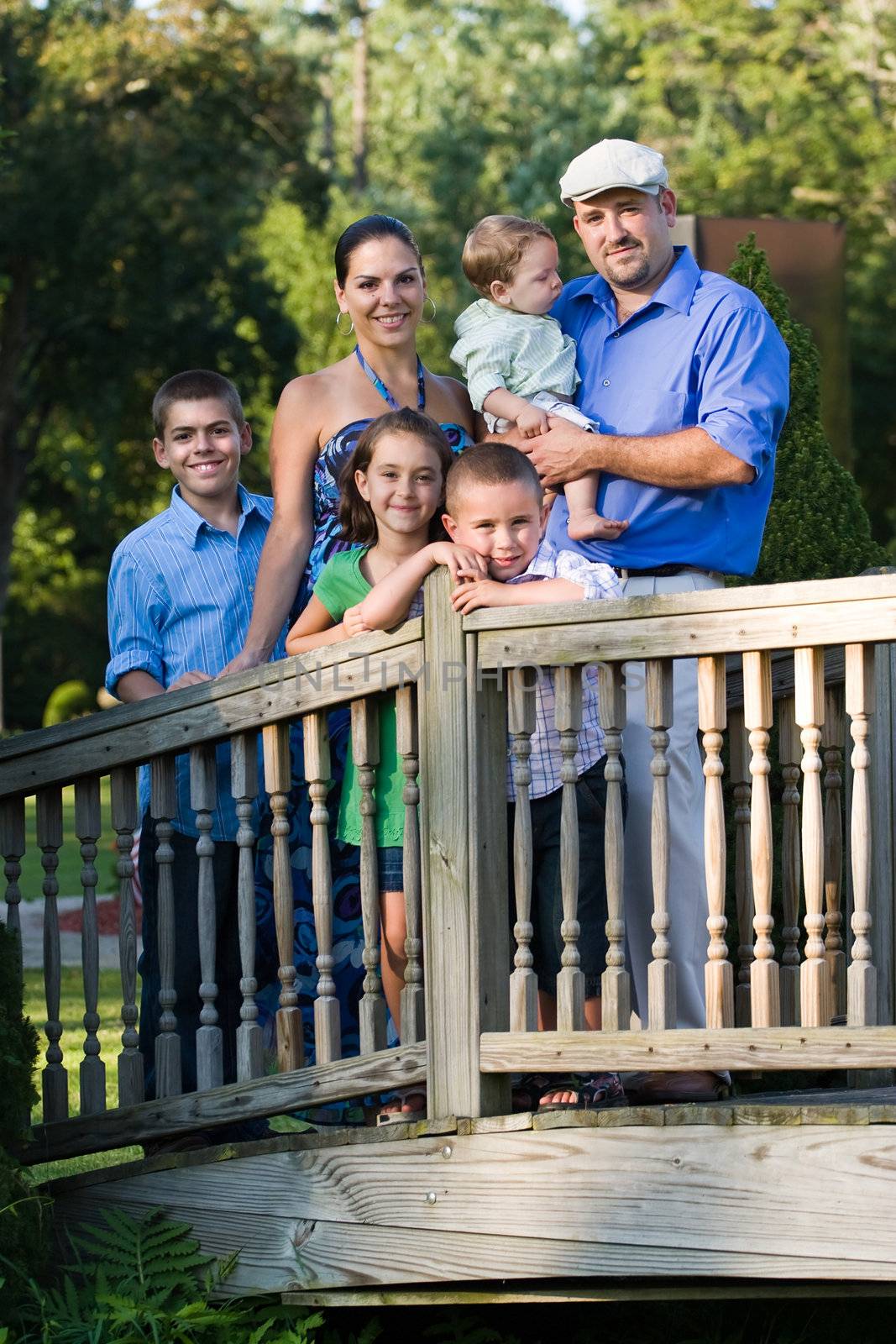 Portrait of an attractive young family with four children posing in a park on a wooden walking bridge.