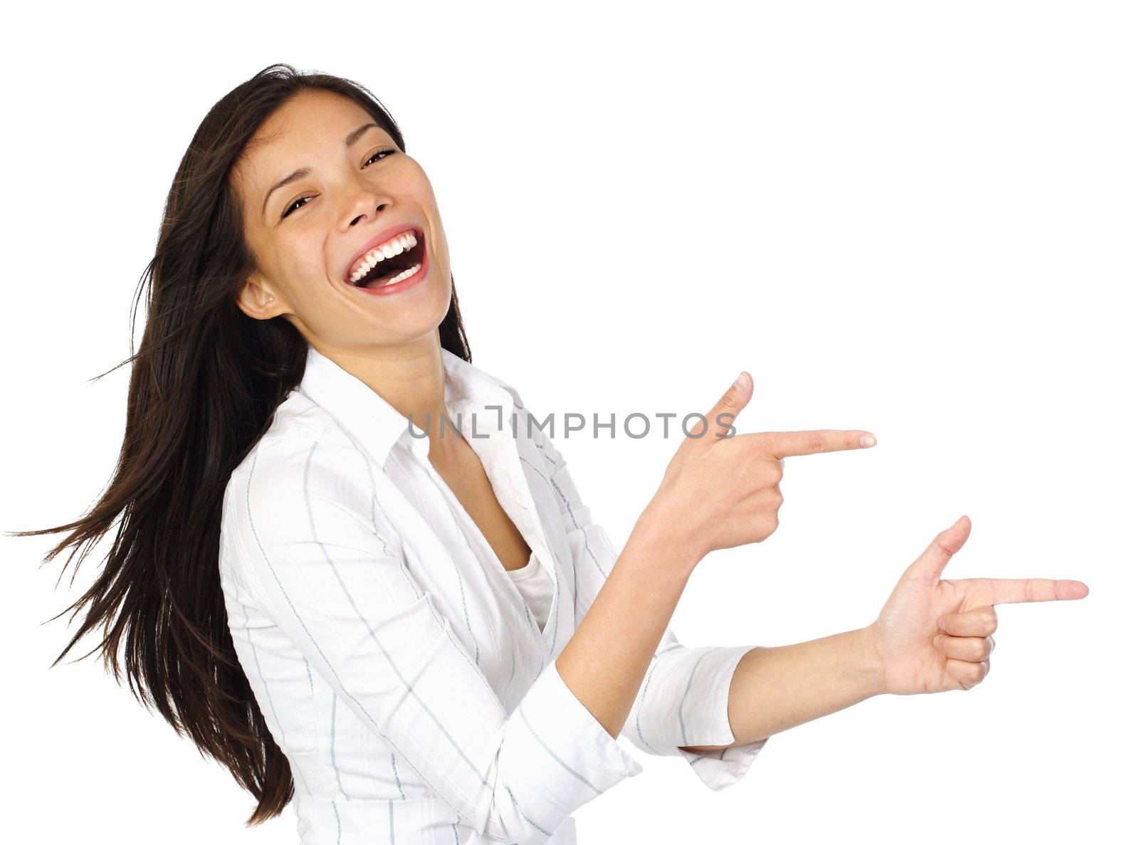 Laughing woman in white pointing at your product while looking at the camera. Isolated on white background. Beautiful mixed asian / caucasian model.