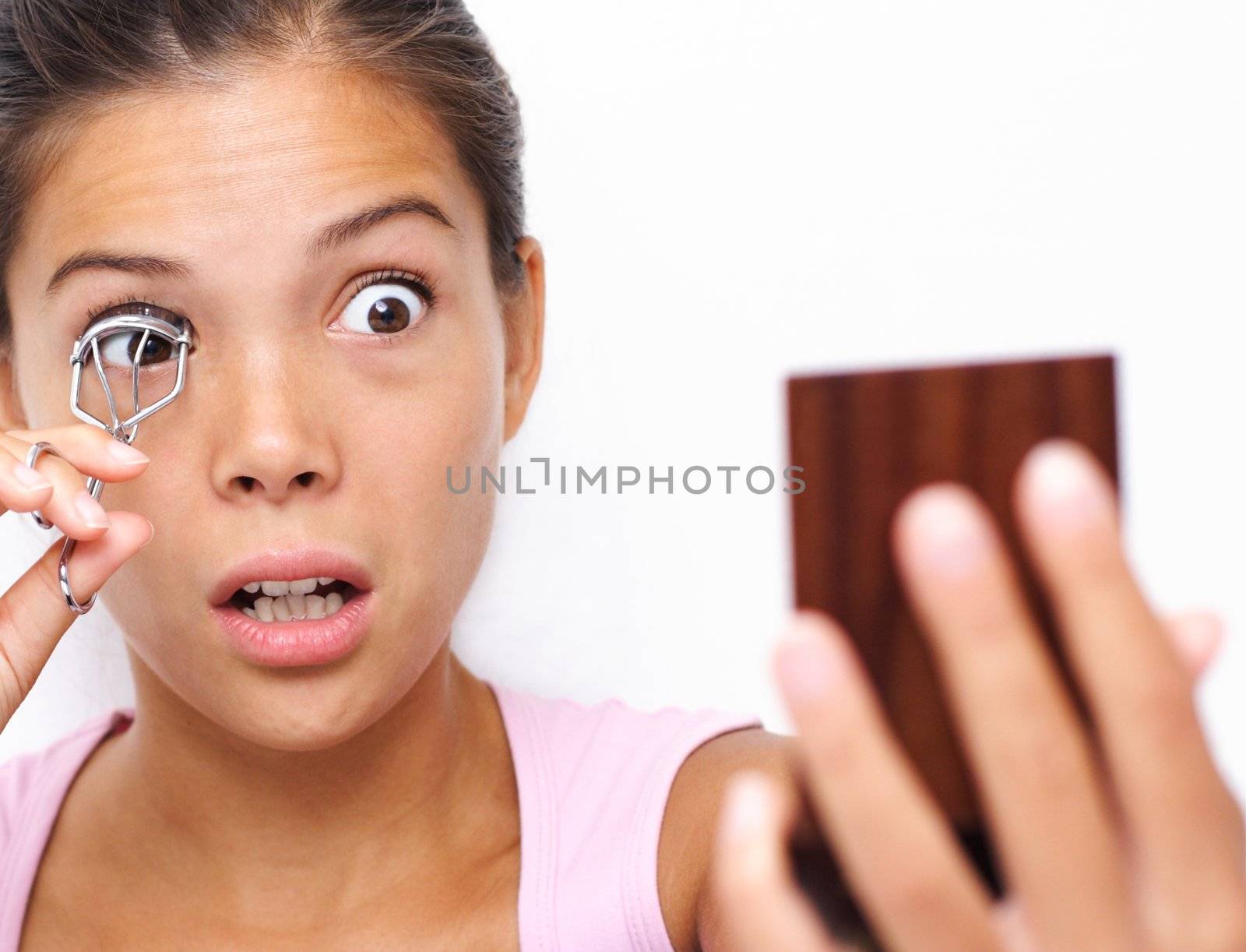 Funny image of woman curling her eyelashes looking in a pocket mirror. Beautiful young asian / caucasian woman.