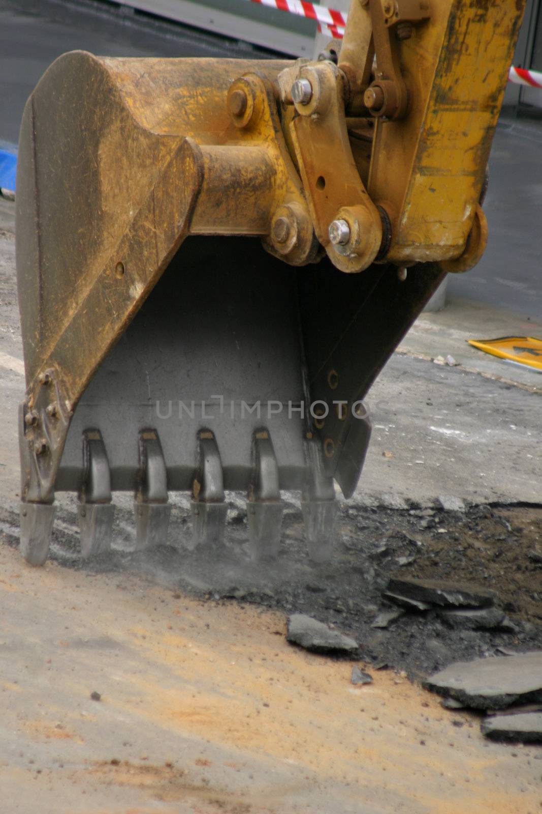 Large steel teeth of the excavator vibrate and shake noisily as they begin to dig up an existing road.