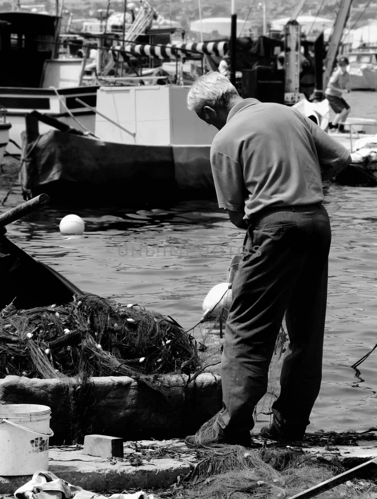 Old man and the sea - fisherman fixing his nets at the fishing village of Marsaxlokk in Malta