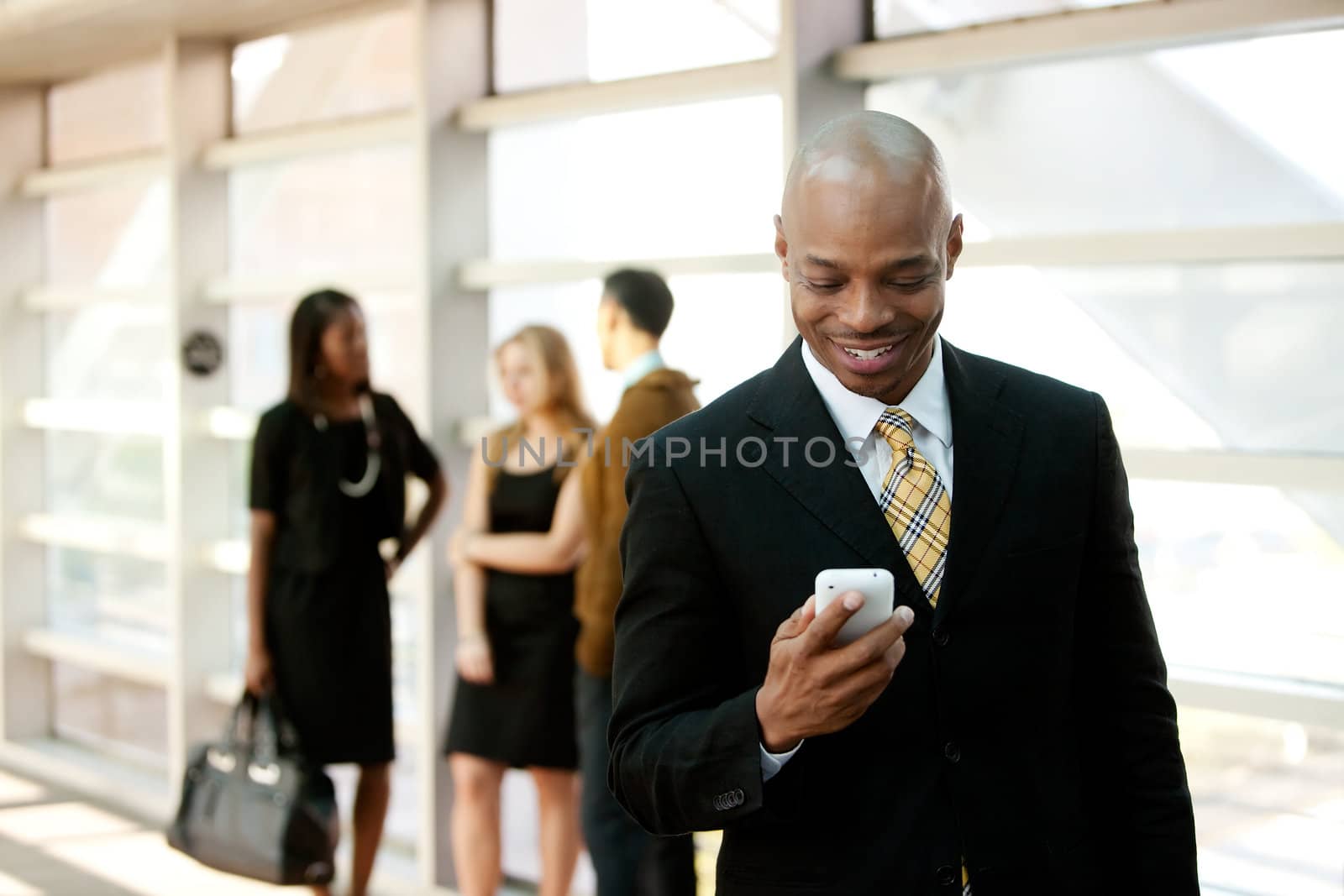 A business man with a smart phone and co-workers in the background