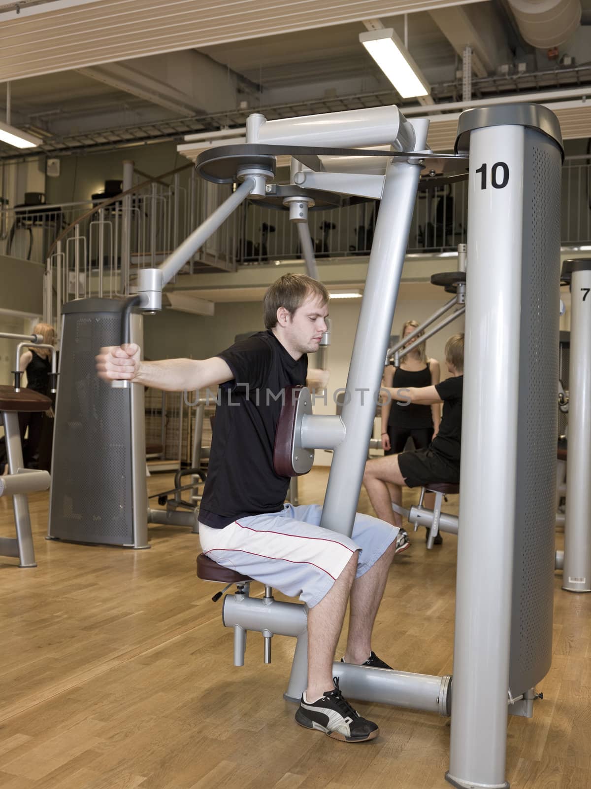 Young man using an exercise machine at a health club with a girl and a boy in the background