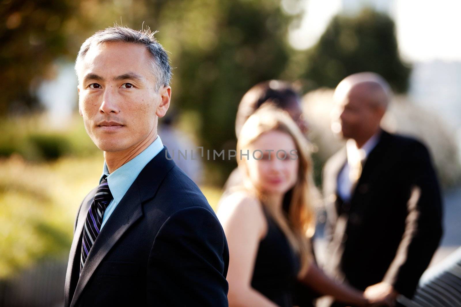 An Asian business man with a serious expression and colleagues in the background