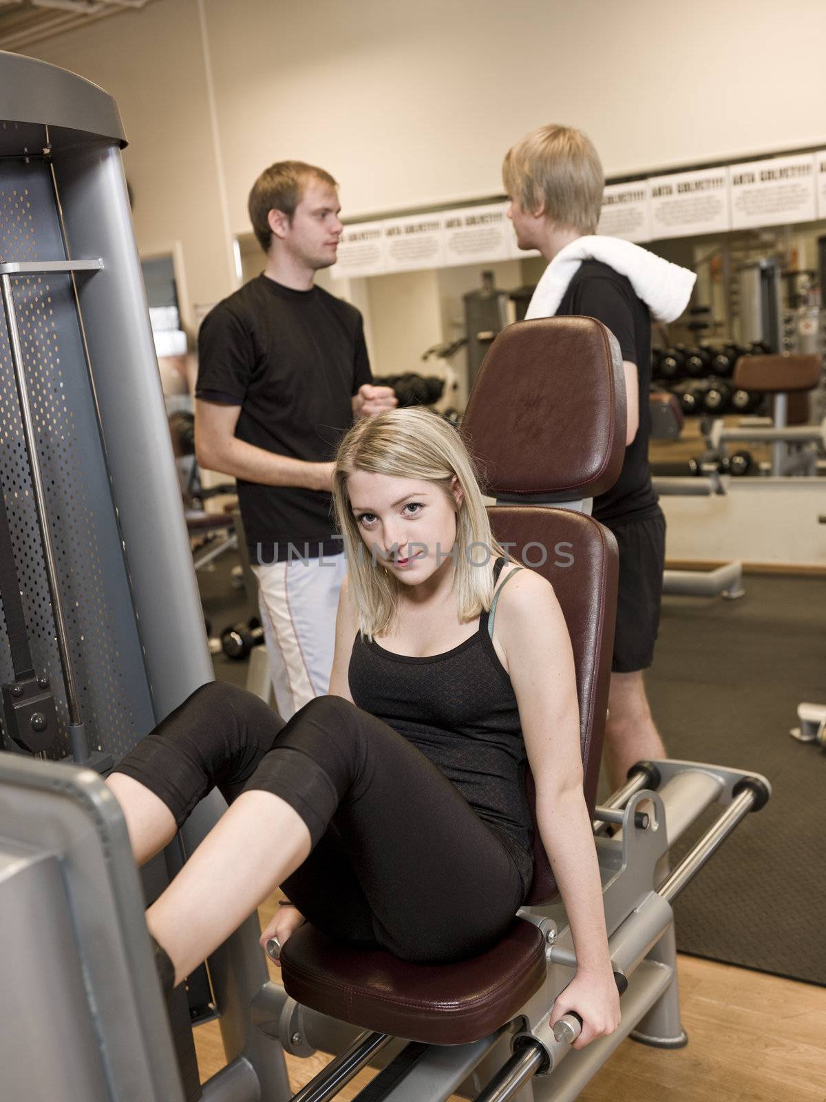 Girl using an exercise machine at a health club with two men in the background