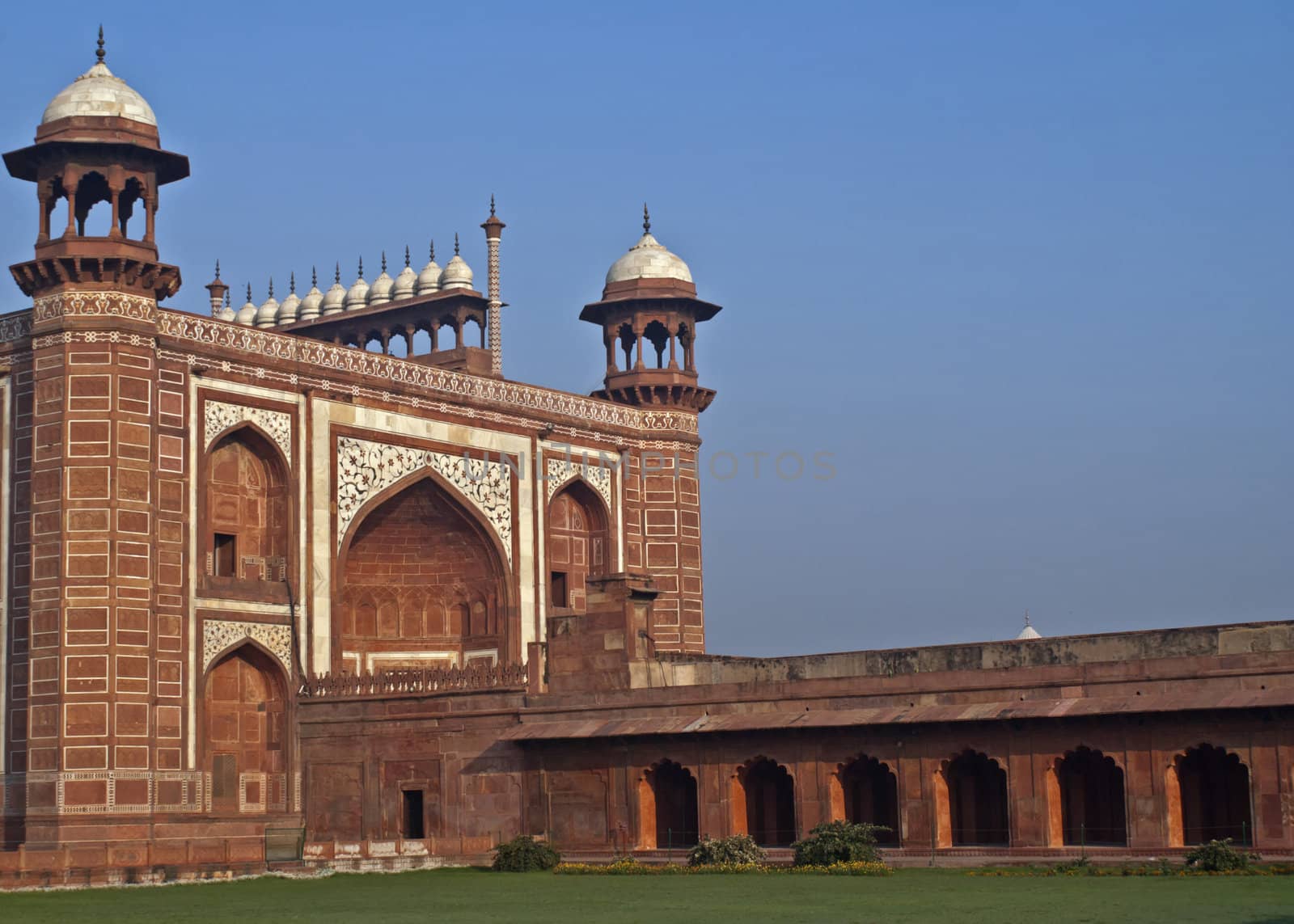 Green lawn, blue skies, red walls, and white marble decorations topped by a line of chhatris.