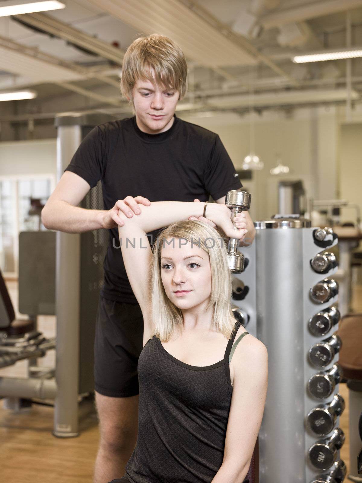 Young man helping a girl lifting weights at a fitness center