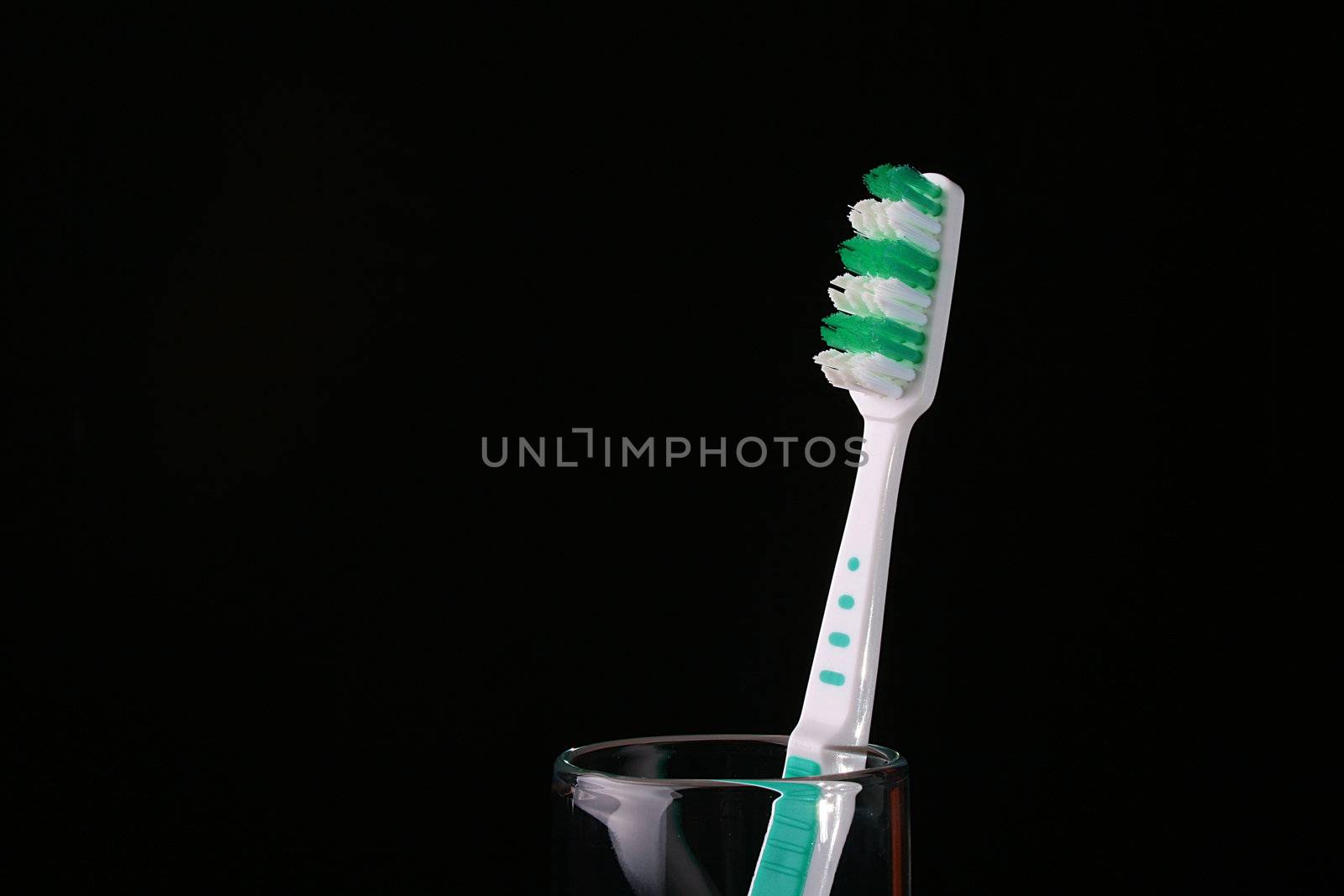 New dark green with white a tooth-brush in a glass on a black background.
