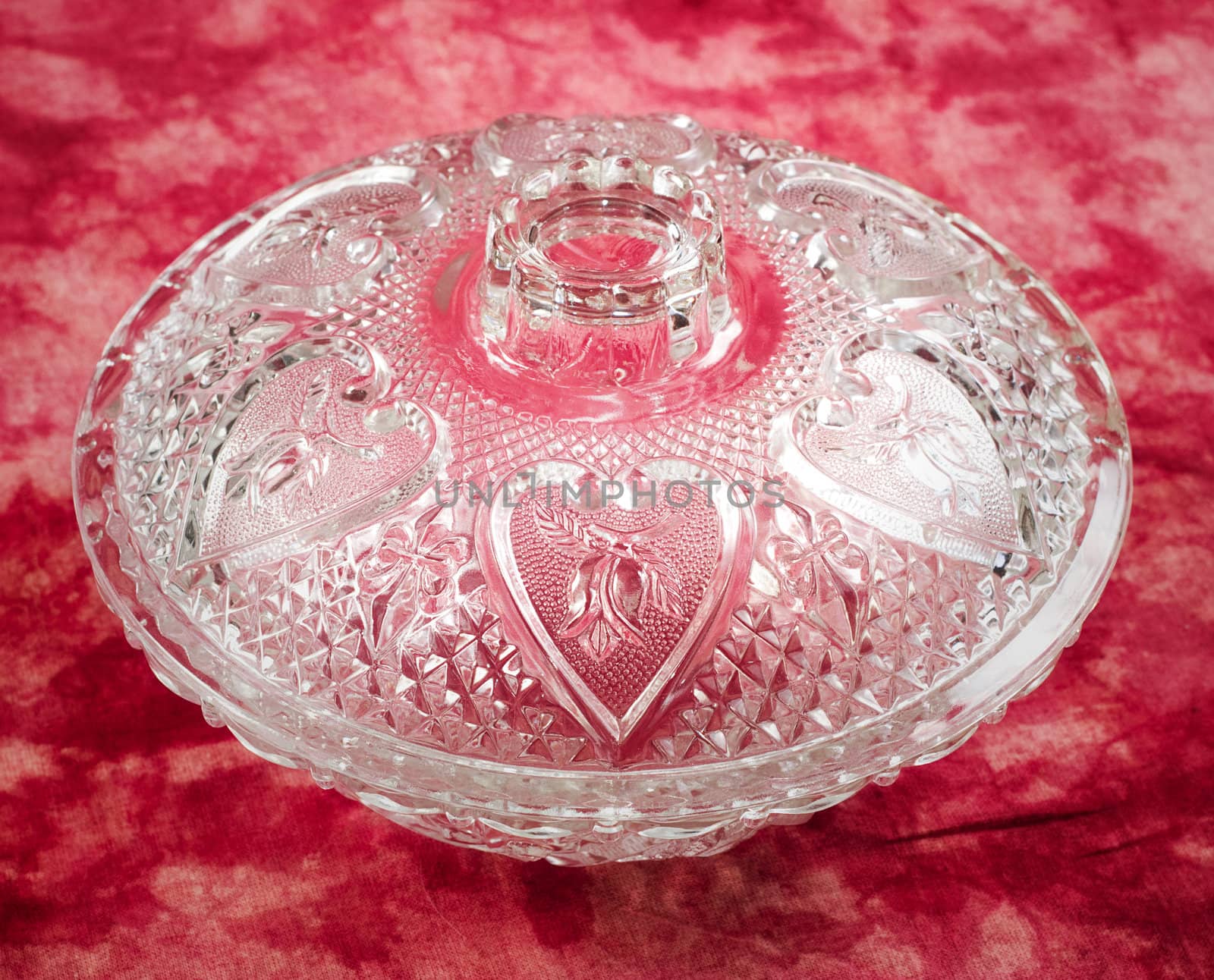A glass candy dish with hearts shot on a red background