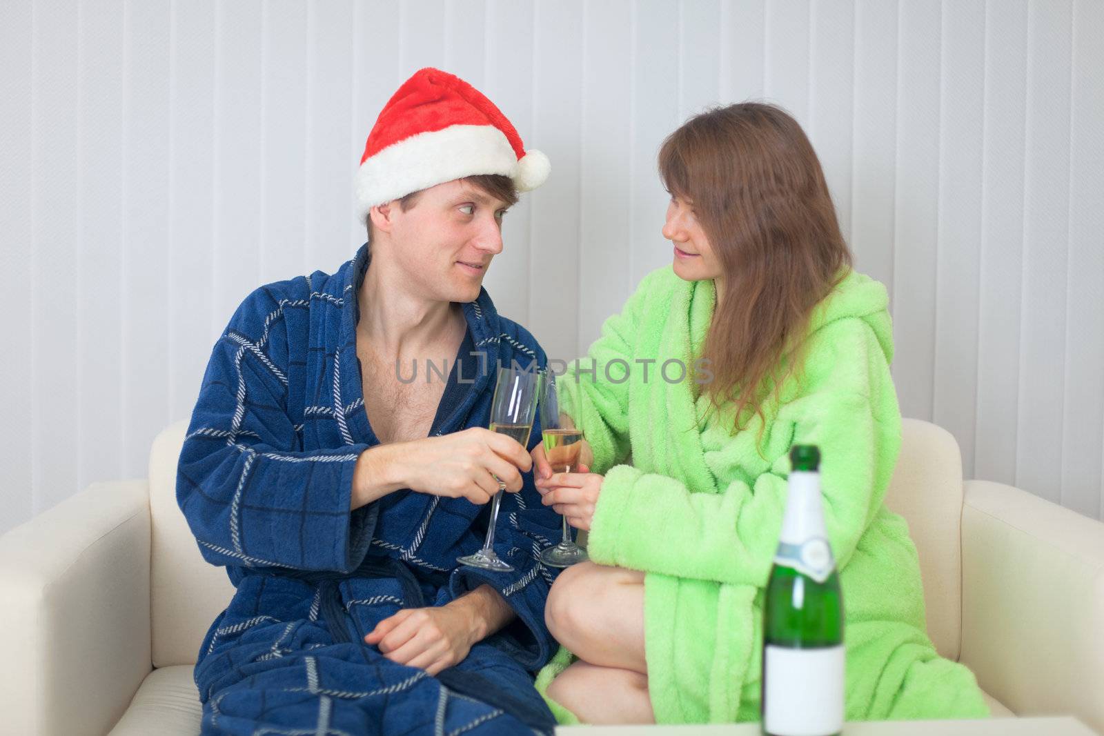 The young couple drinks sparkling wine in dressing gowns on a sofa
