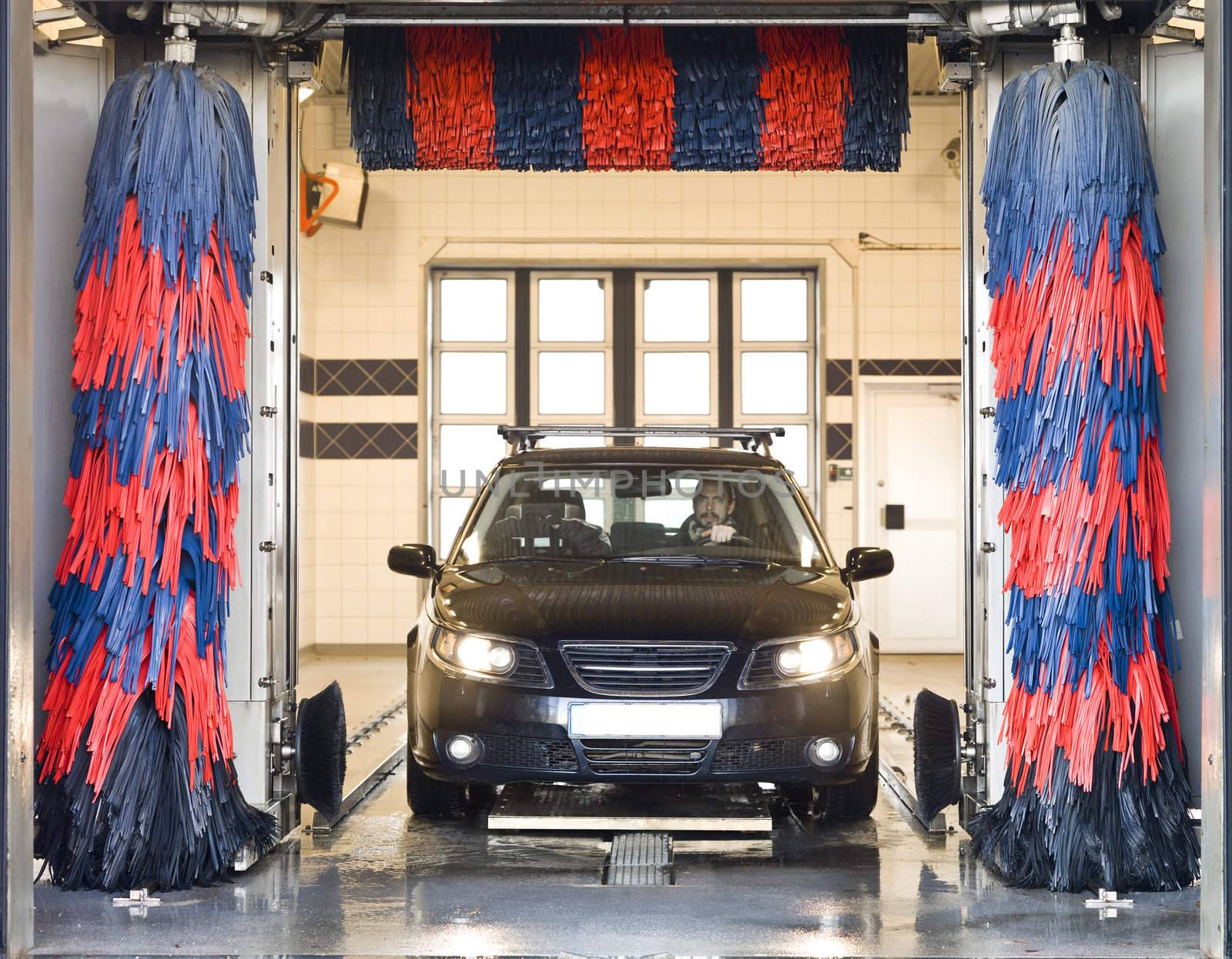 Black car with a male driver washing the car in a car wash